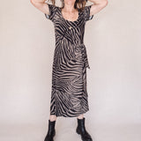 Woman wearing a zebra print dress with black boots on a plain background