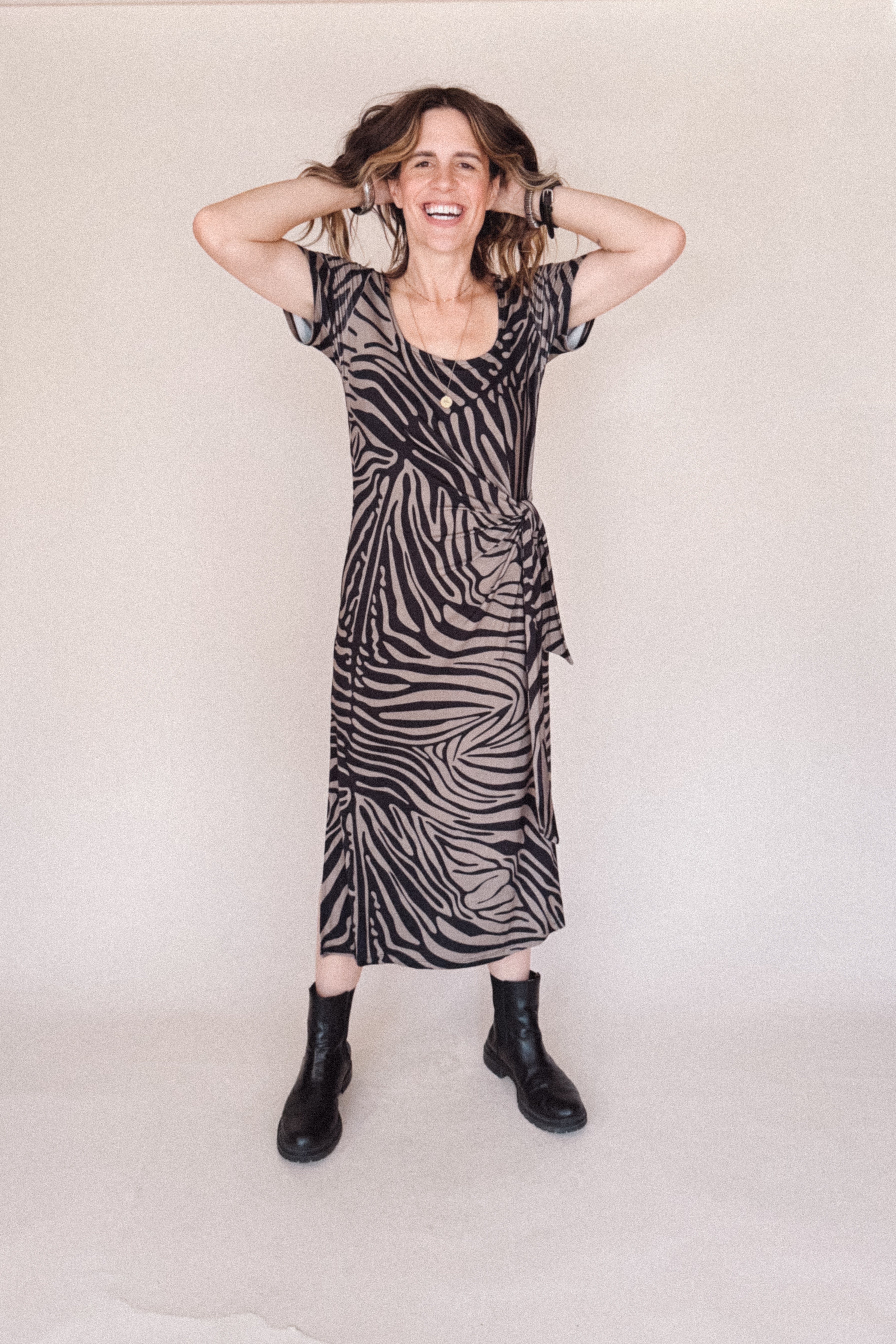 Woman wearing a zebra print dress with black boots on a plain background