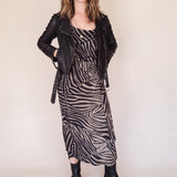 Woman wearing a zebra print dress with a black leather jacket on a plain background