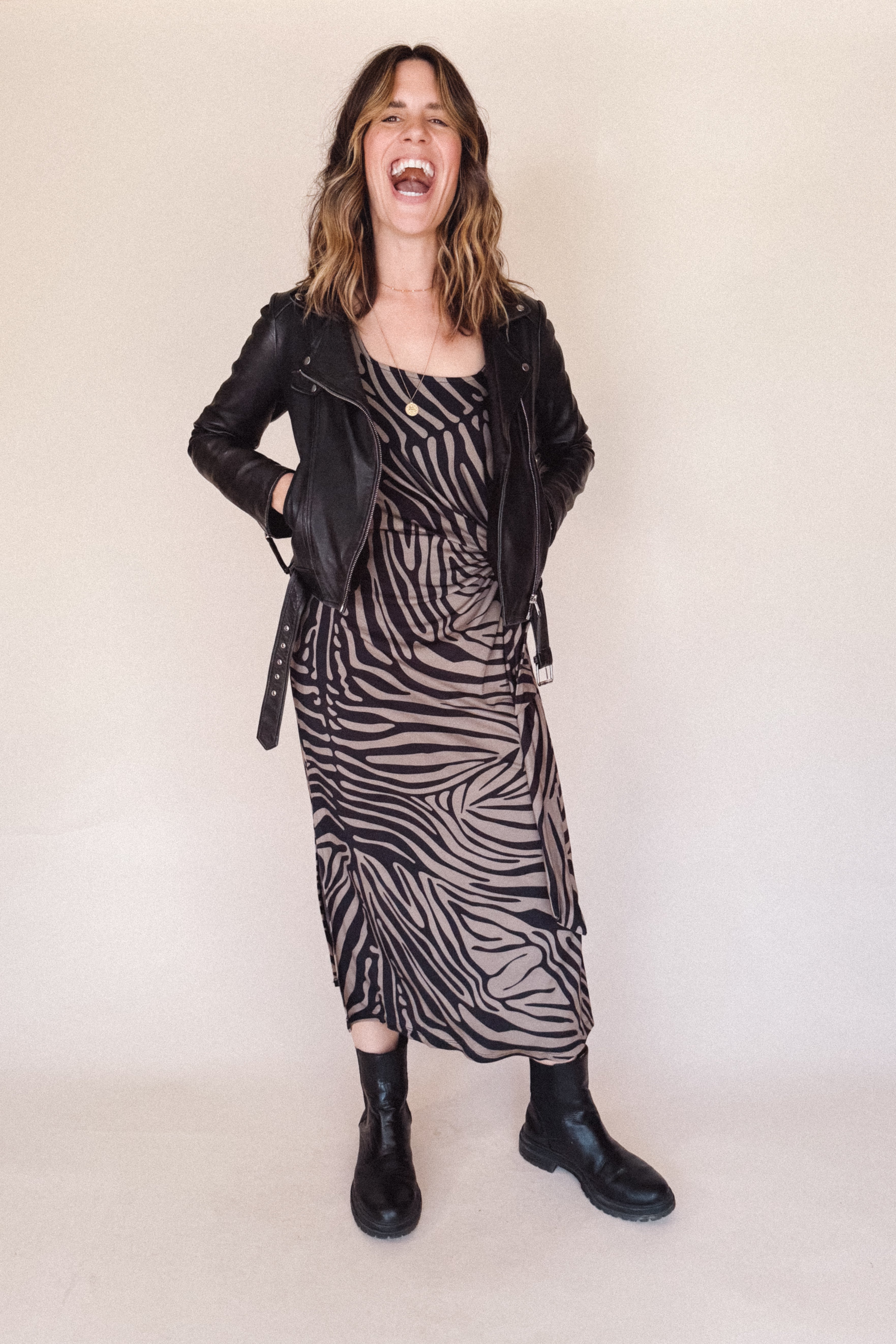 Woman wearing a zebra print dress with a black leather jacket on a plain background