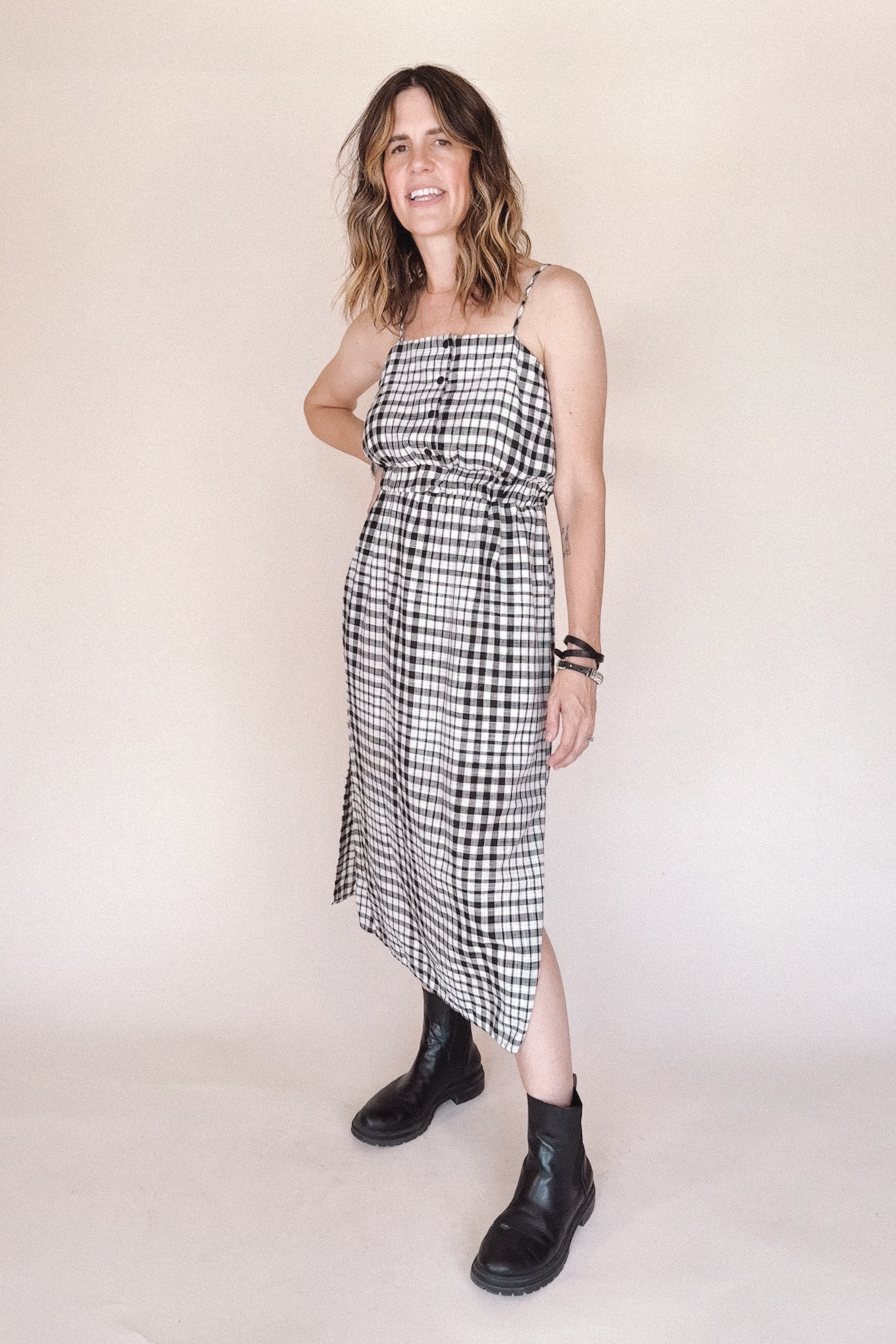 Woman wearing a black and white checkered dress with black boots on a plain background
