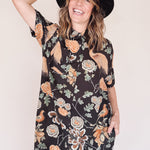 Woman wearing crane-print short sleeve button-up mini shirt dress with collar and side pockets, holding hat