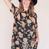 Woman wearing crane-print short sleeve button-up mini shirt dress with collar and side pockets, holding hat