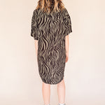 Person wearing a zebra pattern dress on a beige background back of her.
