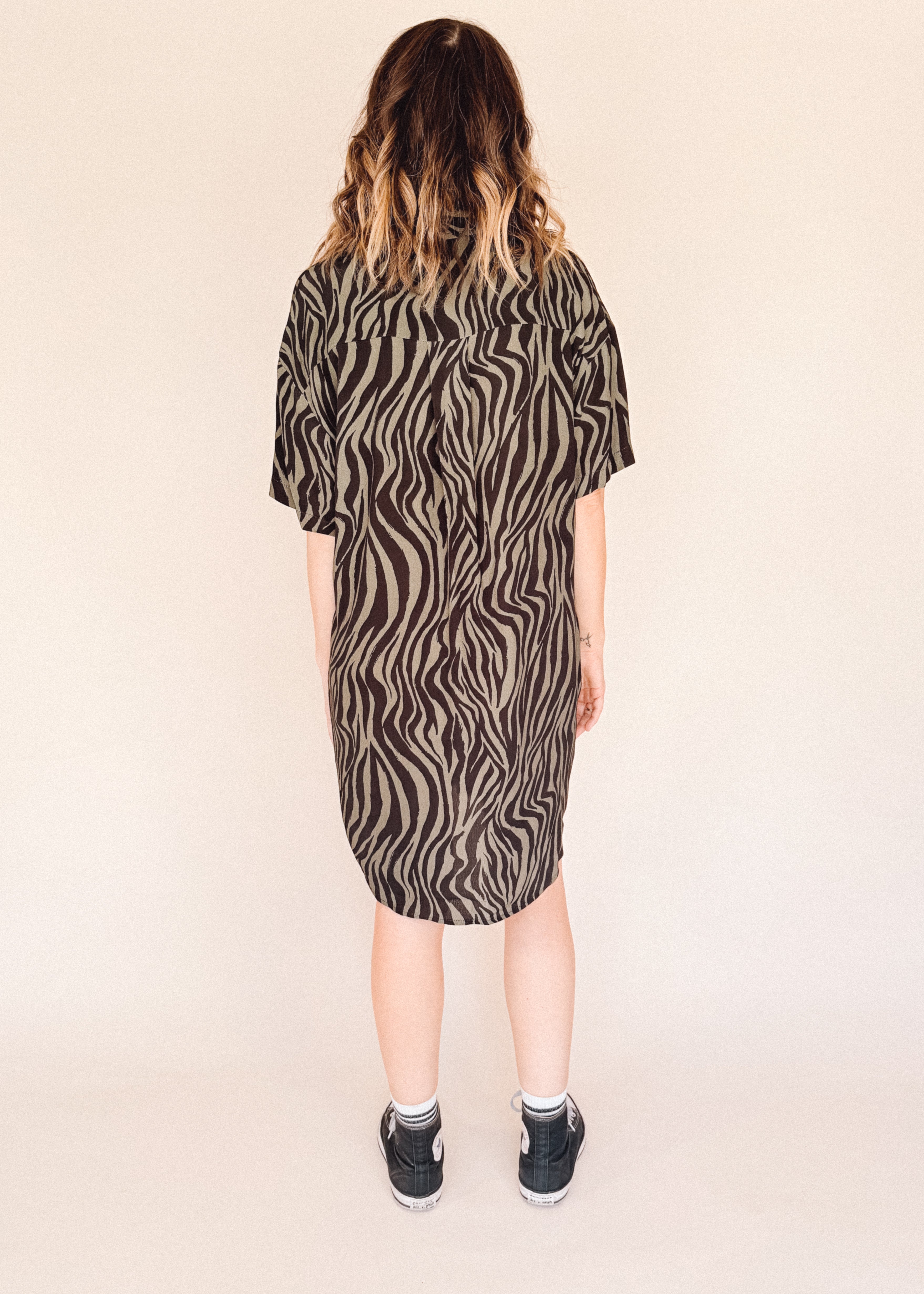 Person wearing a zebra pattern dress on a beige background back of her.