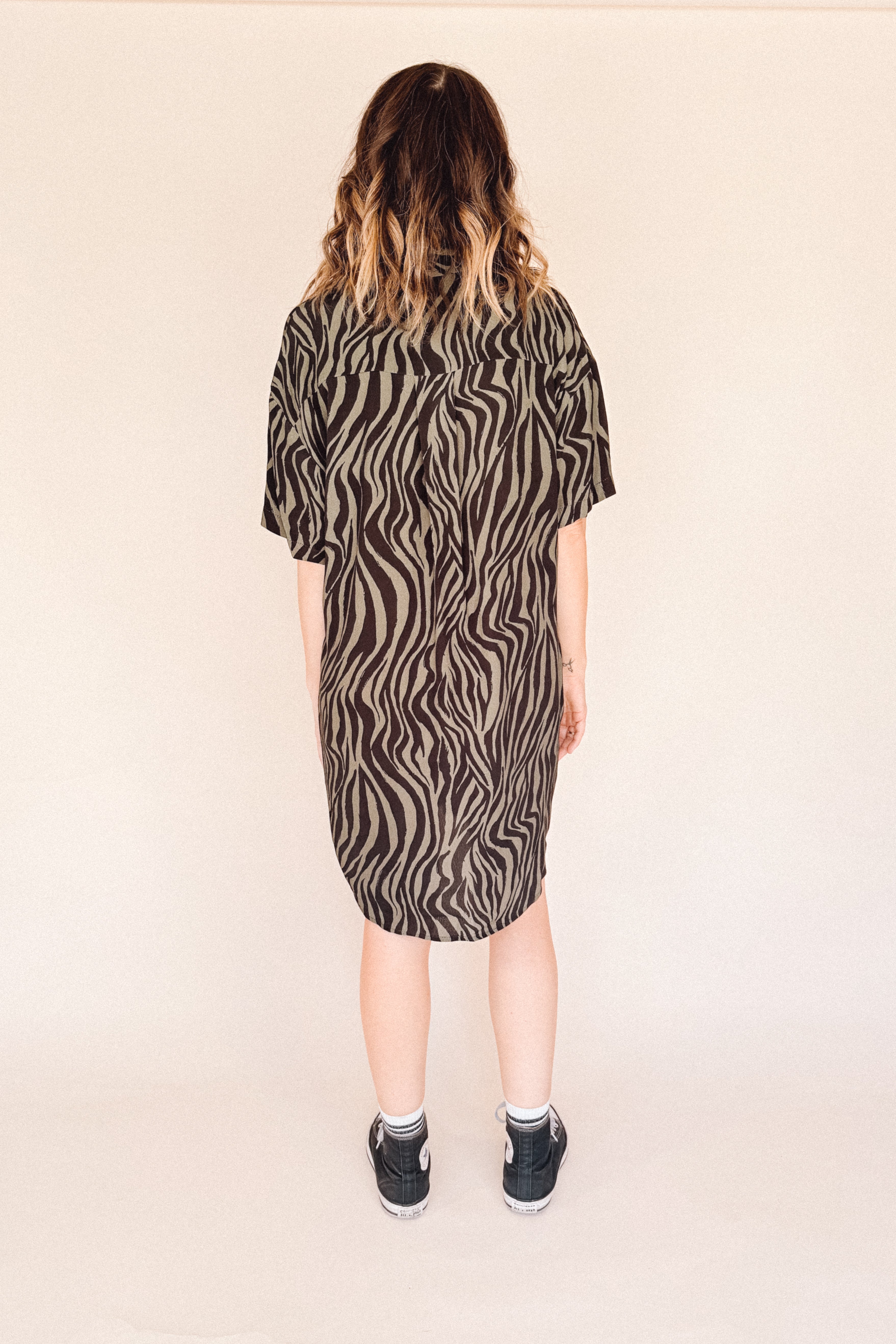 Person wearing a zebra pattern dress on a beige background back of her.