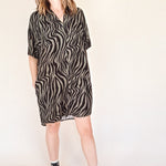 woman wearing a black and olive zebra print button up mini shirt dress with black high-top sneakers on a beige background