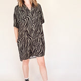 woman wearing a black and olive zebra print button up mini shirt dress with black high-top sneakers on a beige background
