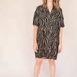 Woman wearing a black and olive zebra print shirt dess dress on a beige background