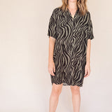 Woman wearing a black and olive zebra print shirt dess dress on a beige background