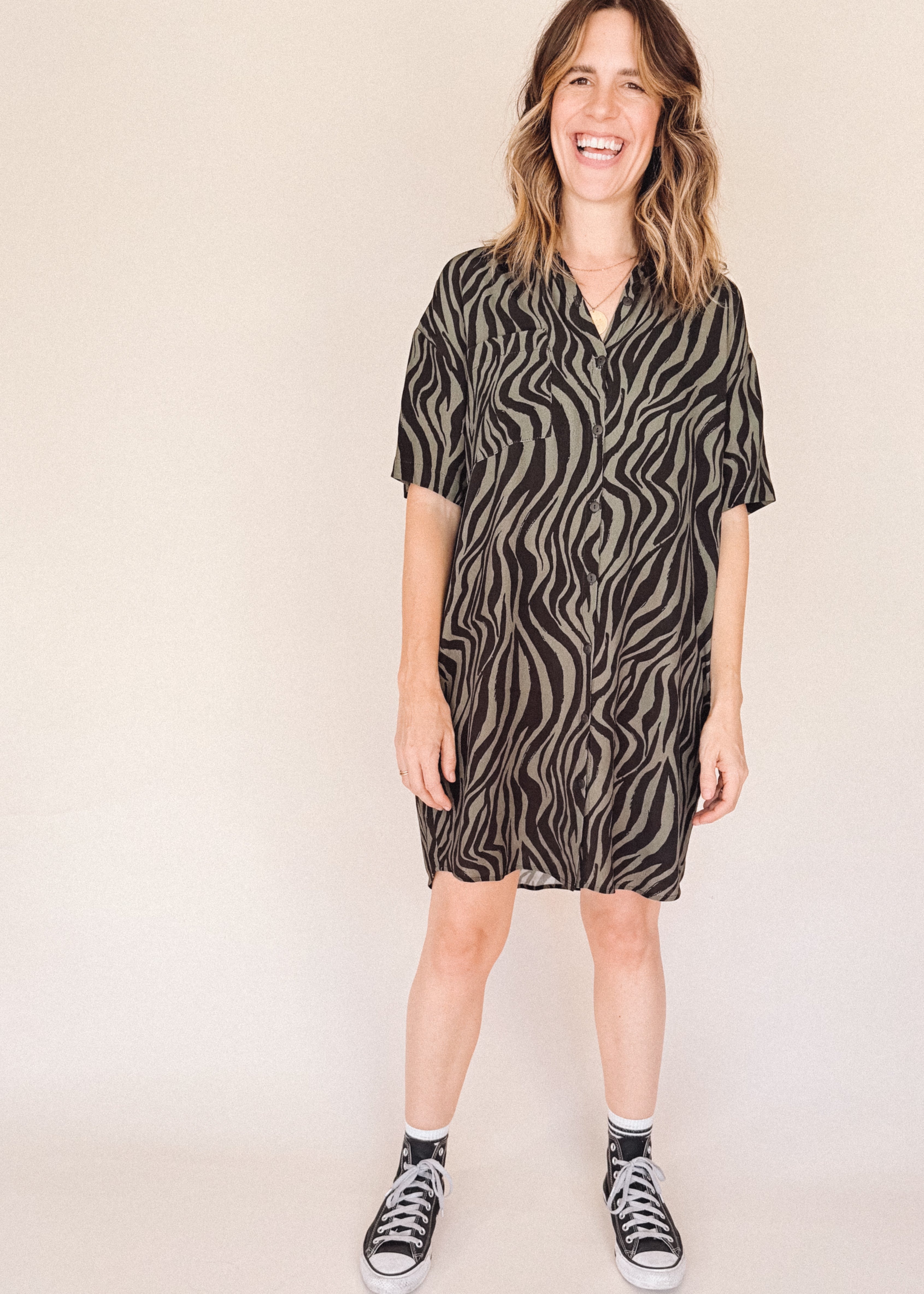Woman wearing a black and olive zebra print shirt dess dress on a beige background