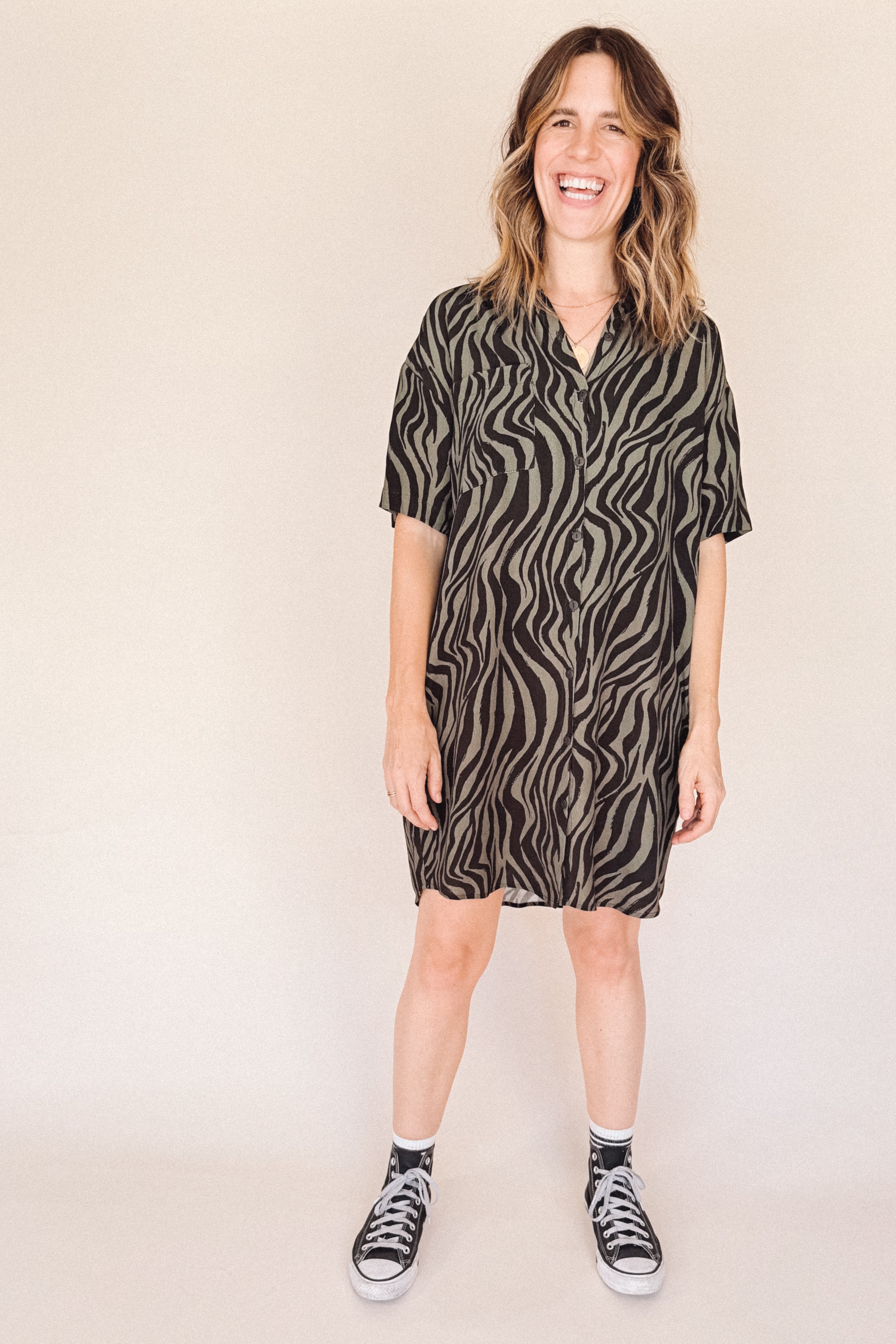Woman wearing a black and olive zebra print shirt dess dress on a beige background