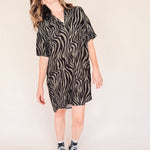 Woman wearing a black and olive zebra print shirt dress on a plain background