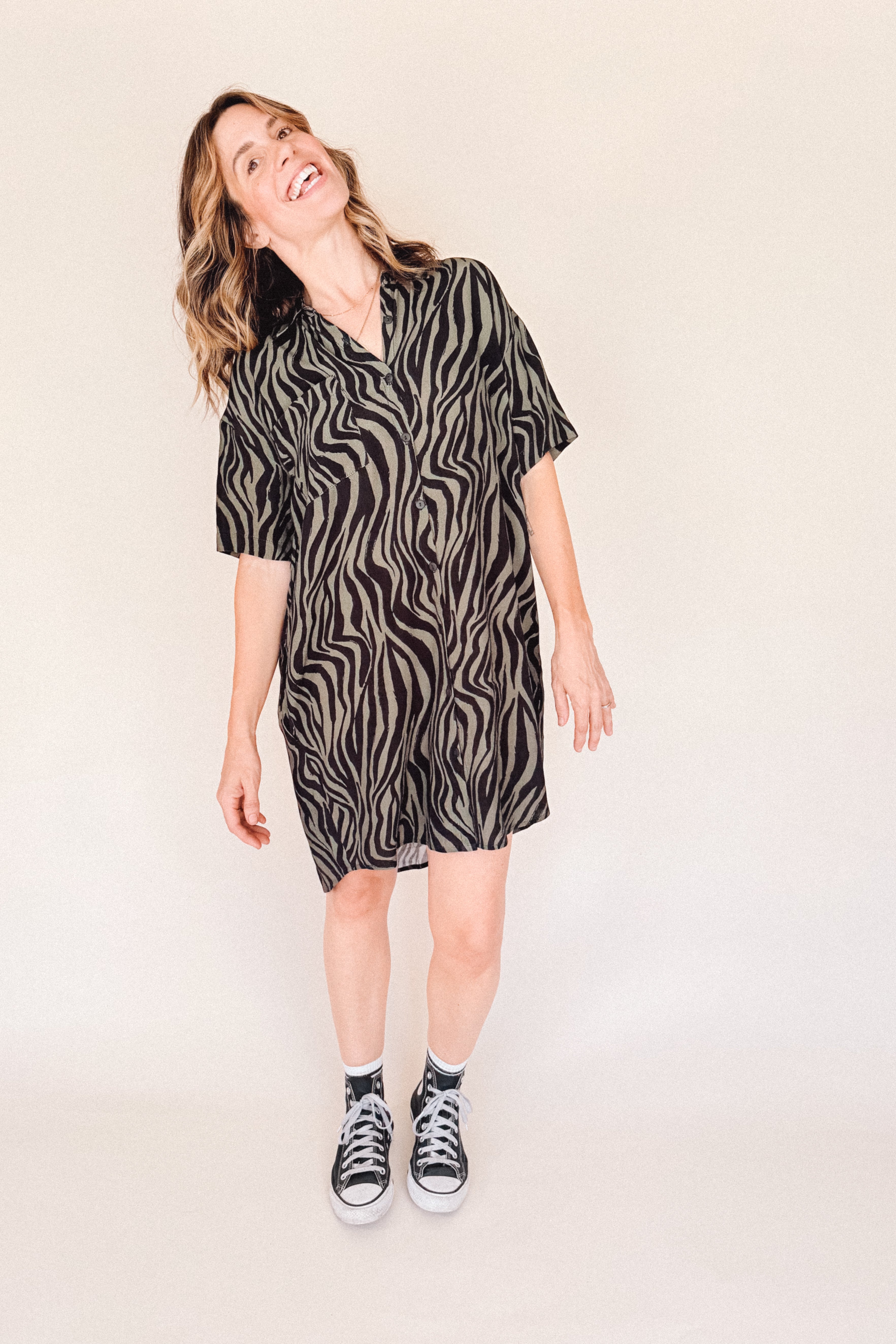 Woman wearing a black and olive zebra print shirt dress on a plain background