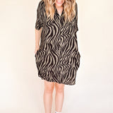 Person wearing a zebra pattern dress with black Converse shoes on a beige background