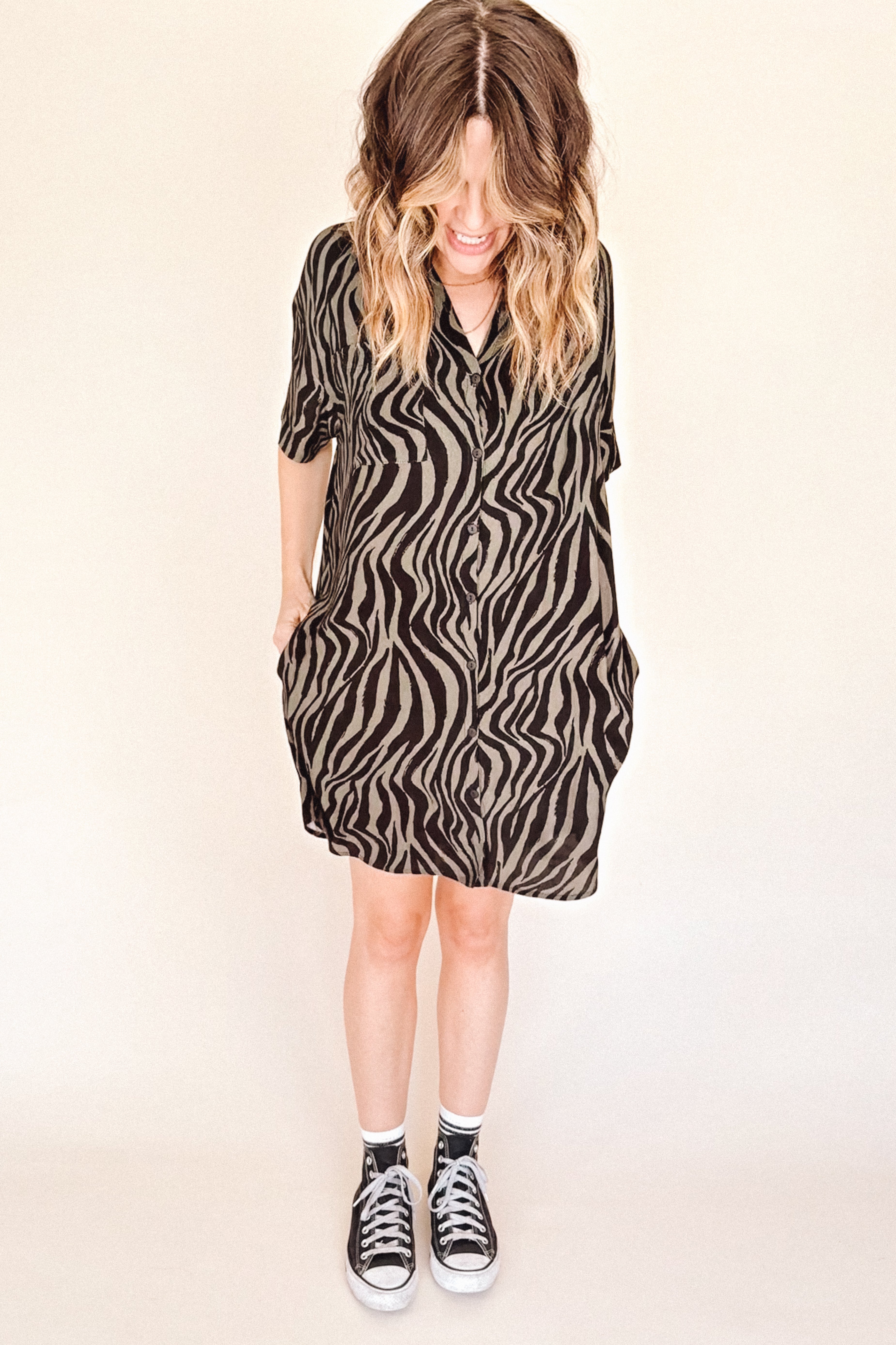 Person wearing a zebra pattern dress with black Converse shoes on a beige background
