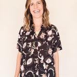 Woman wearing a black eye printed shirt dress close up against a beige background