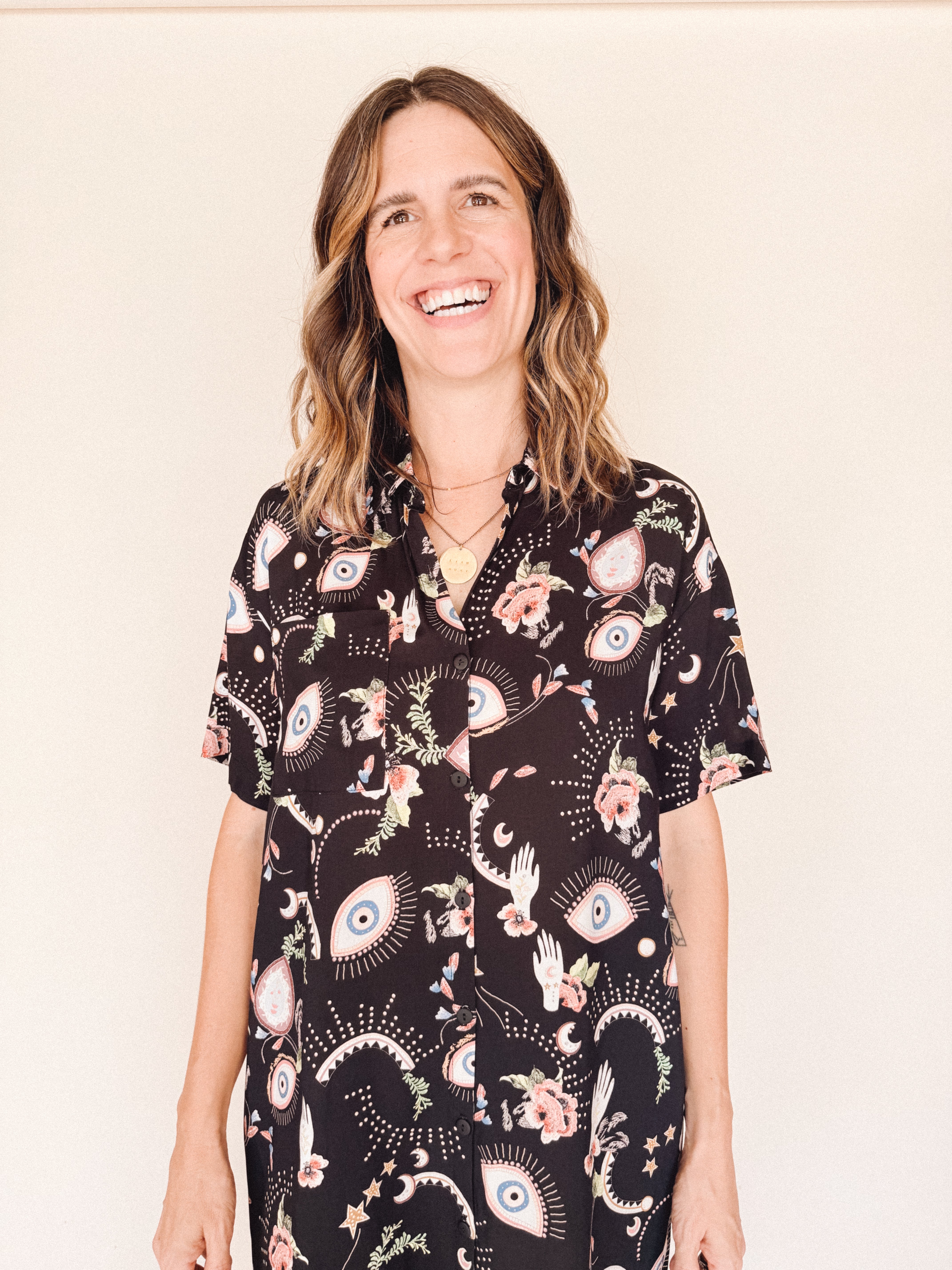 Woman wearing a black eye printed shirt dress close up against a beige background