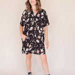 Woman wearing a black eye printed shirt dress with black high-top sneakers on a beige background