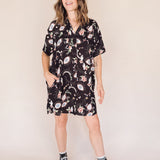 Woman wearing a black eye printed shirt dress with black high-top sneakers on a beige background