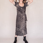 Woman wearing a zebra print dress with black boots on a plain background