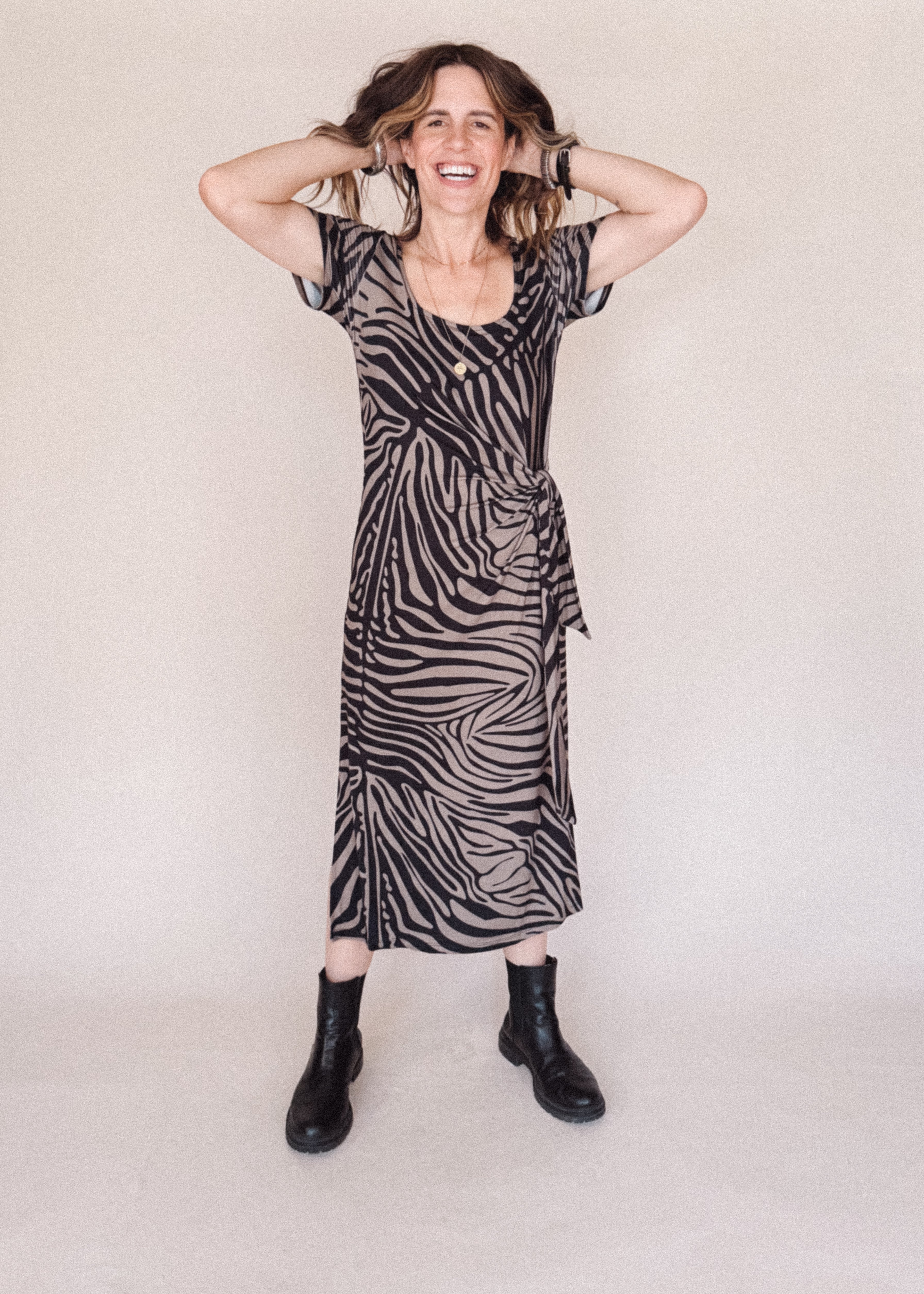 Woman wearing a zebra print dress with black boots on a plain background
