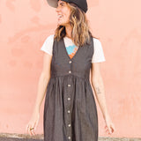 Woman wearing a gray dress over a white shirt with a colorful design, standing against a pink wall.