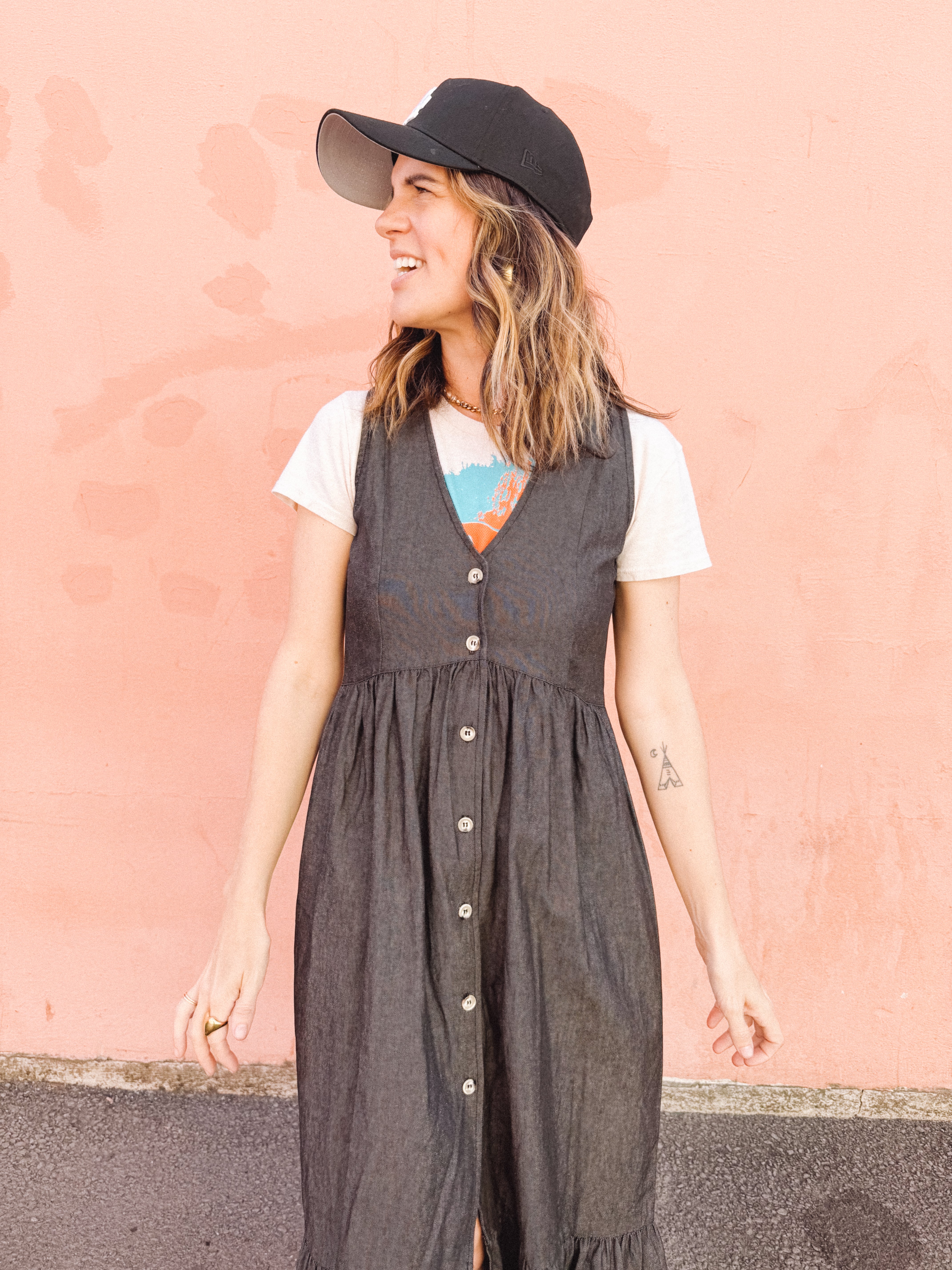 Woman wearing a gray dress over a white shirt with a colorful design, standing against a pink wall.