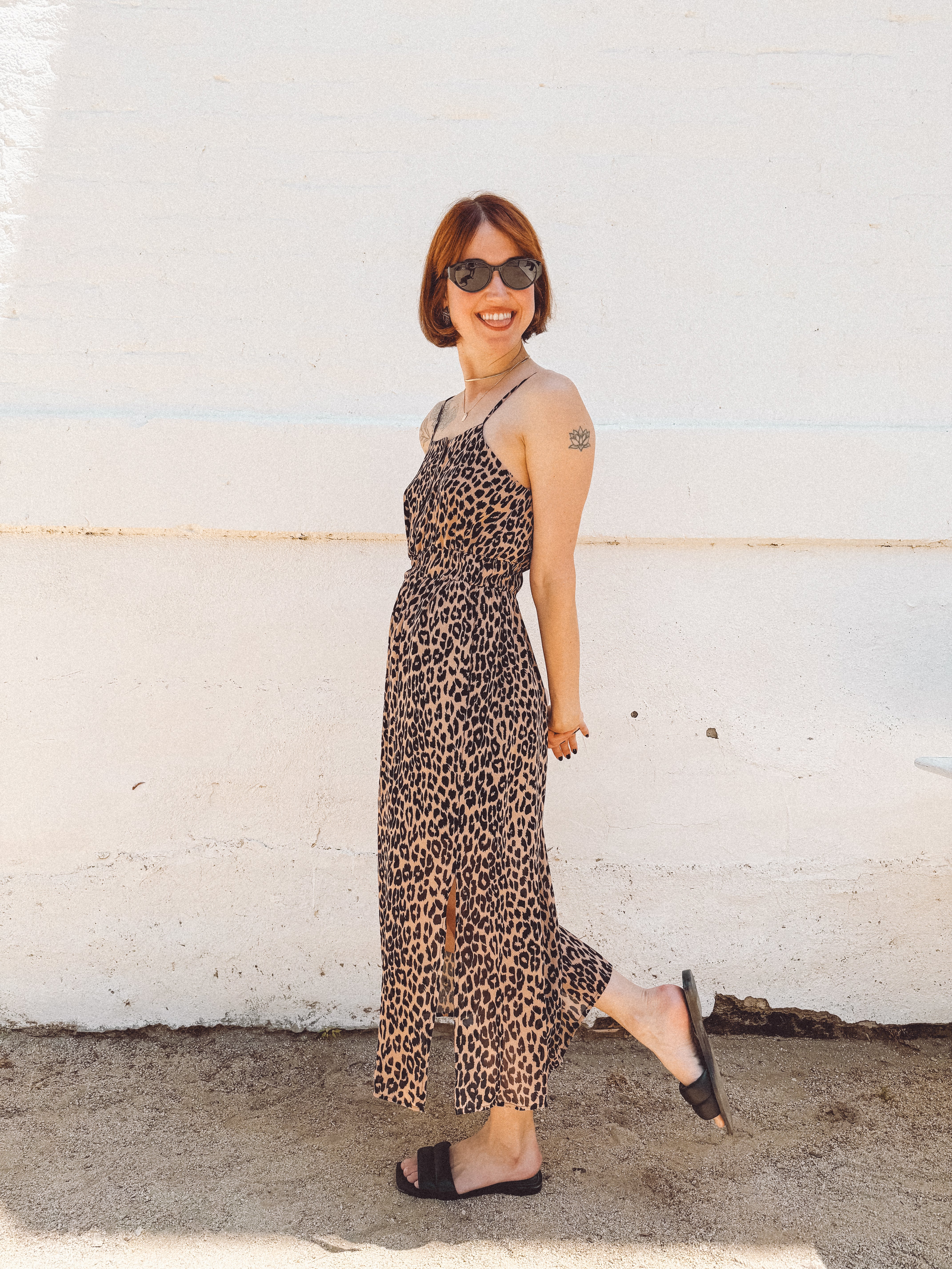 girl wearing leopard elastic waist spaghetti strap midid dress with side slits and sticking out her tongue
