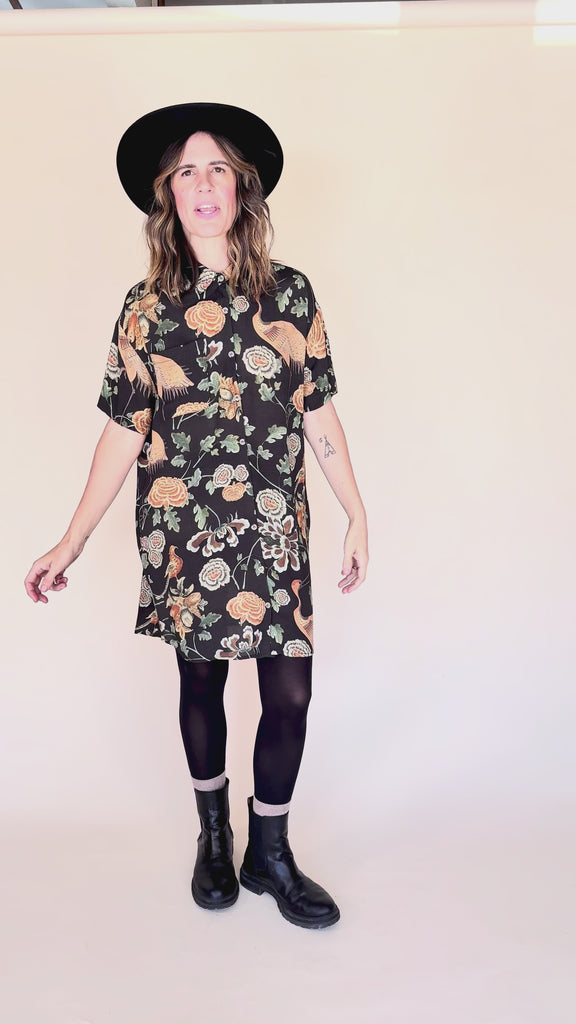 Woman wearing crane-print short sleeve button-up mini shirt dress with collar and side pockets twirling around